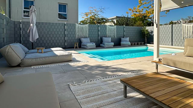 Ein moderner Außenbereich mit einem Pool, umgeben von Liegestühlen und Sonnenschirmen, sowie einem Holztisch auf einer Terrasse.